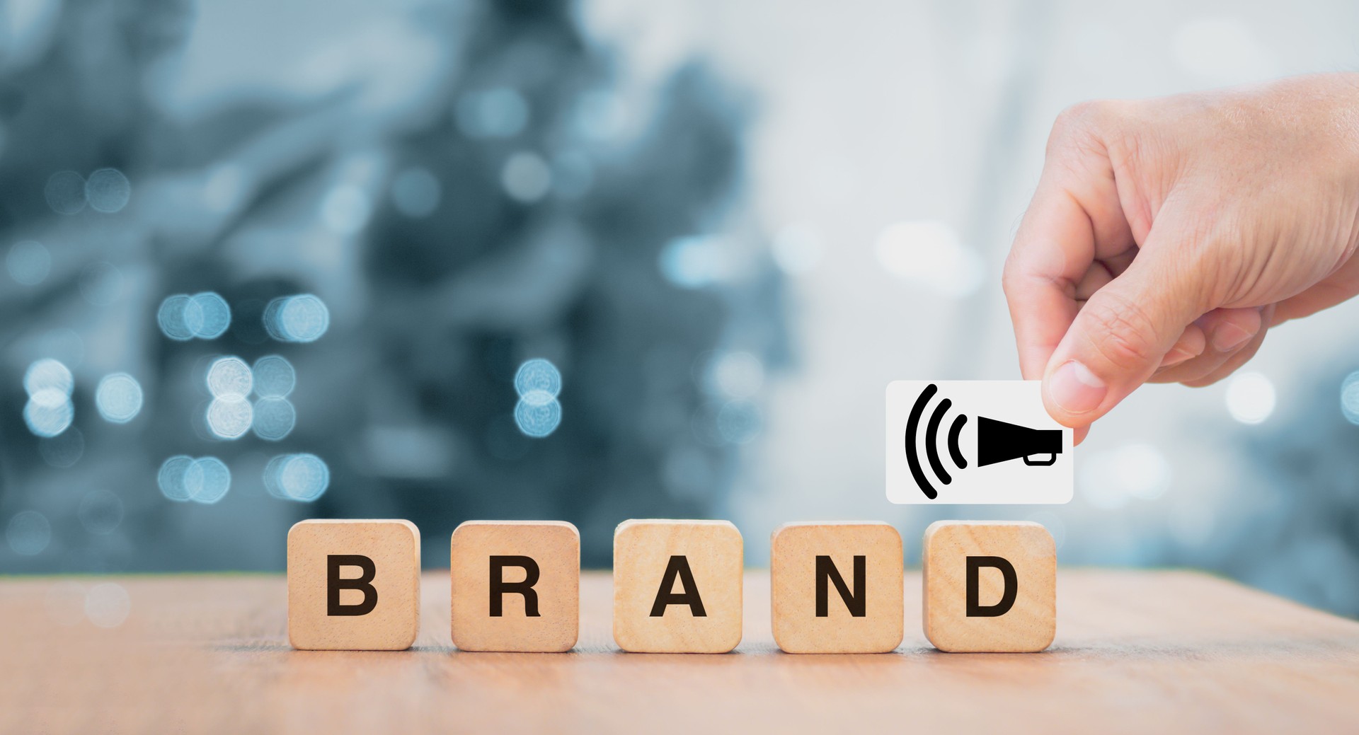 Hand of male putting megaphone symbol on wood cube block with word BRAND on wooden table. Brand building for success concept  as build brand awareness concept